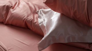 A close up of two pink silk pillowcases on matching silk bedding
