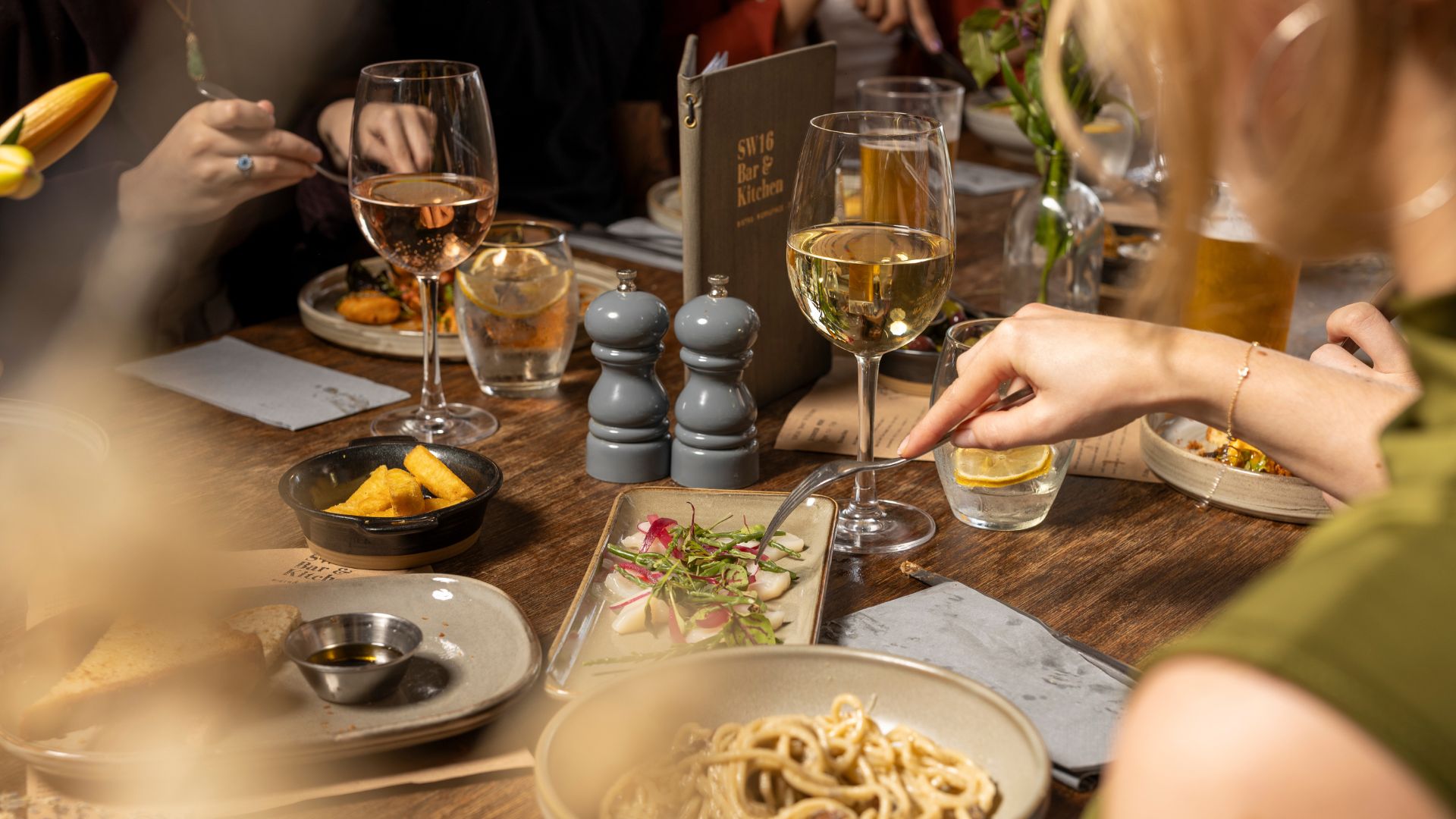 an image of a supper club in full swing - there are plates of pasta and wine on a rustic brown table