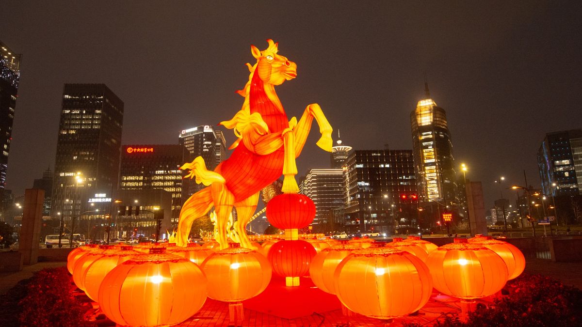 黃色和紅色的馬形狀的巨大燈籠照亮了城市天際線前的一個小公園。