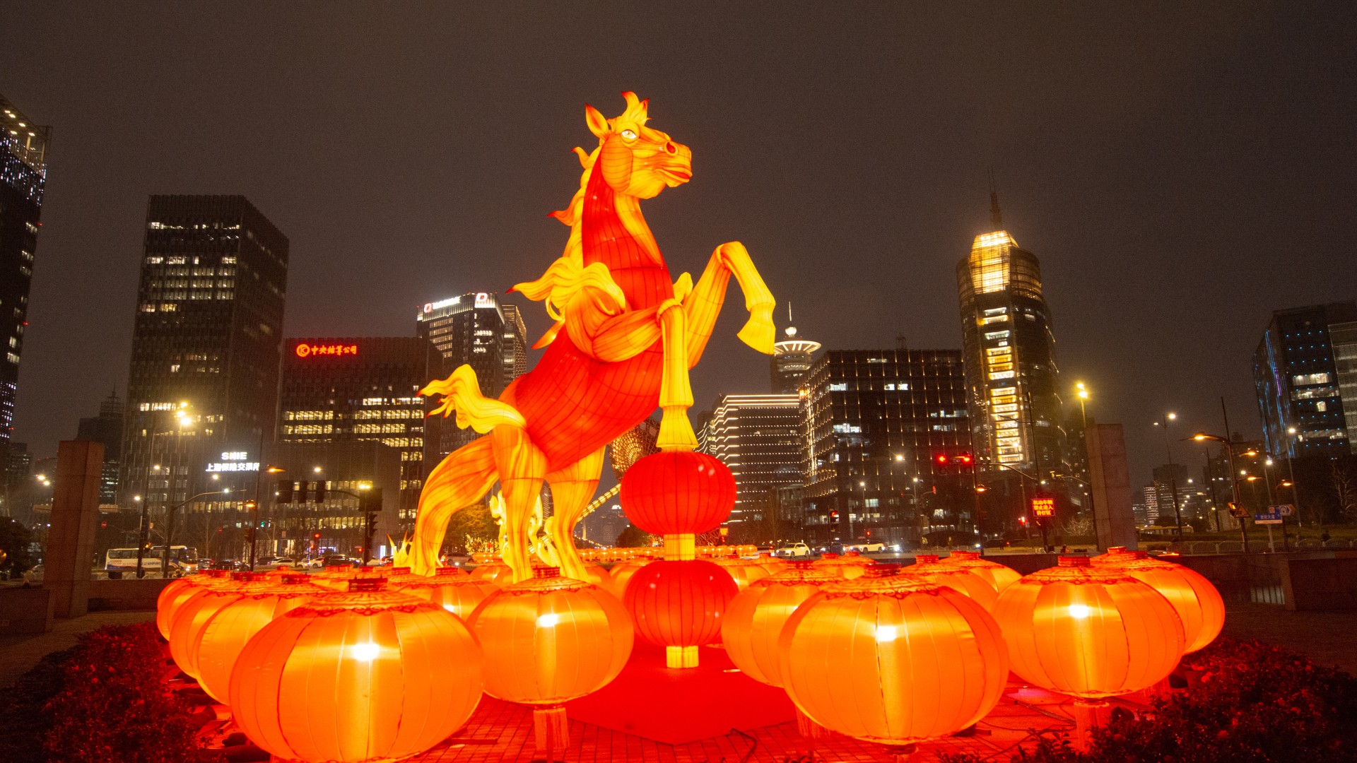 فانوس كبير على شكل حصان أصفر وأحمر يضيء حديقة صغيرة أمام أفق المدينة