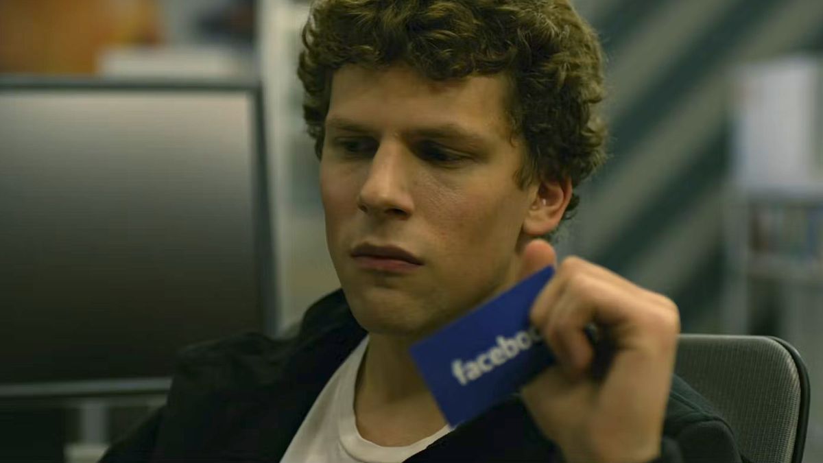 Jesse Eisenberg as Mark Zuckerberg holding a Facebook business card during The Social Network, one of the best movies on HBO Max.