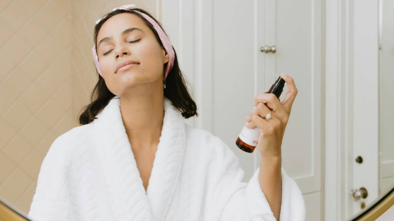 A woman in a white robe spraying her face in the mirror