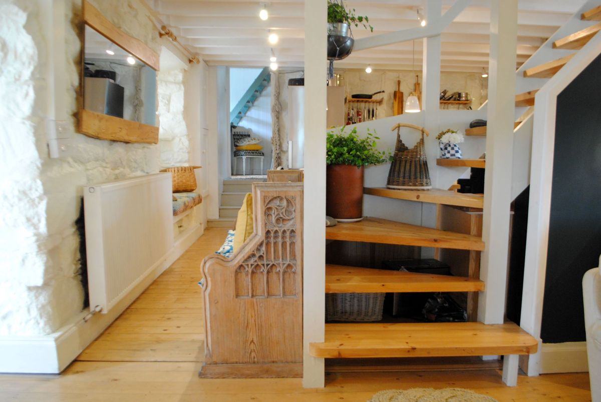The hallway has white stone walls and a wooden staircase and flooring with a white radiator along one wall with a long rectangular mirror above it