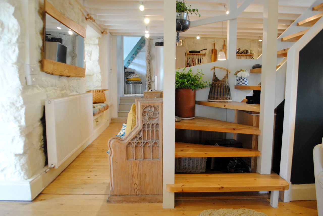 The hallway has white stone walls and a wooden staircase and flooring with a white radiator along one wall with a long rectangular mirror above it