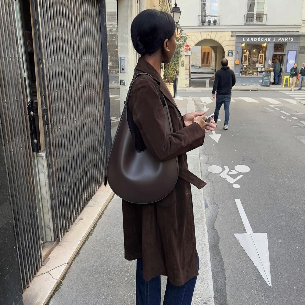Influencer @sylviemus_ wears dark wash, slim fit jeans with a brown suede trench coat and a brown leather bag.