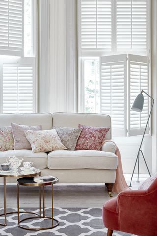 white tier on tier shutters in living room with white sofa and pink cushions shutter store