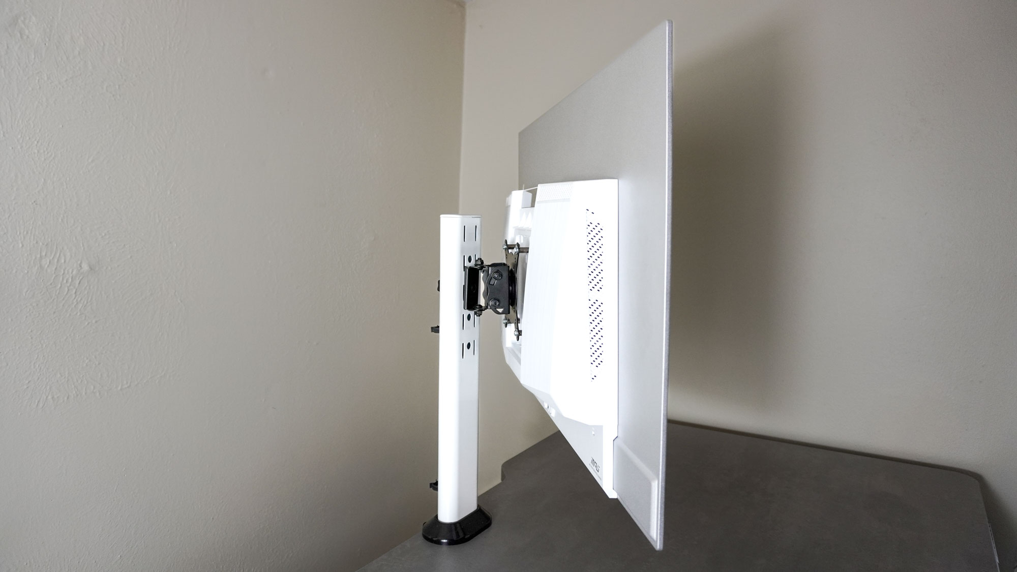 The MSI MPG 321URXW QD-OLED monitor mounted to the back of a desk and tilted to the side