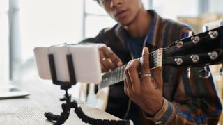 Man playing guitar, looking at phone.