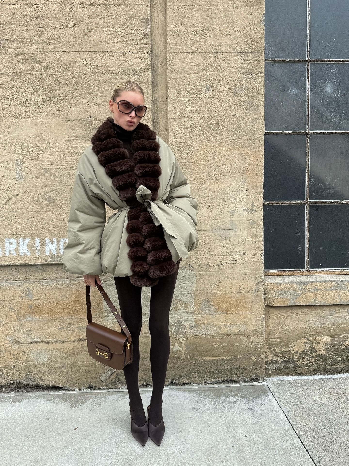 Elsa Hosk wearing a fur-trimmed parka, brown tights, and brown Alaia satin mules