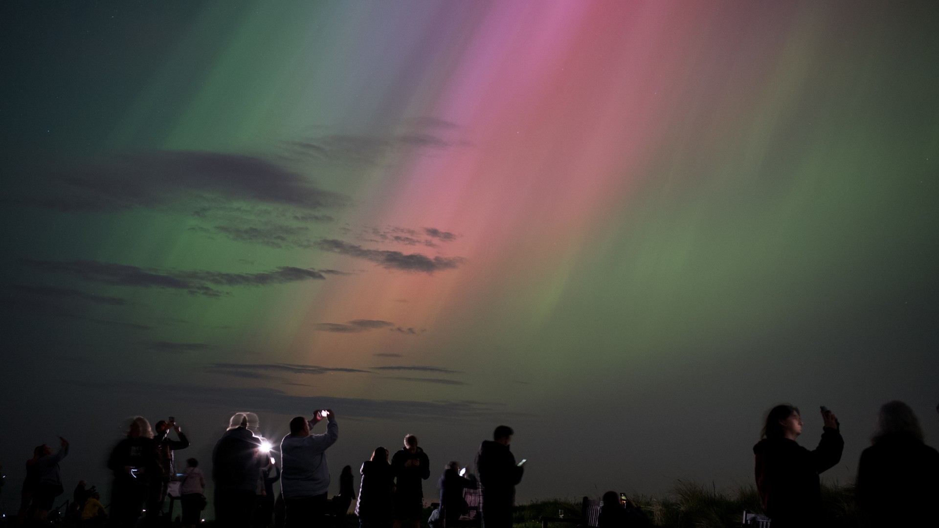a crowd of people taking pictures of the sky is silhouetted against colorful wisps of light above