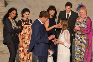 Humphrey (Kris Marshall) and Martha (Sally Bretton) stand on the beach, with Humphrey holding a ring box in his hand, in a shot taken slightly from above them. Their friends and colleagues are gathered around them in a semi-circle: Charlie Woods (Jade Harrison), Zoe Williams (Melina Sinadinou), Esther Williams (Zahra Ahmadi), Kelby Hartford (Dylan Llewellyn) and Margo Martins (Felicity Montagu)