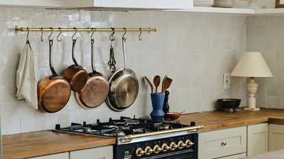 A white kitchen with wooden worktops, a gas cooker, and a pan rack on the wall
