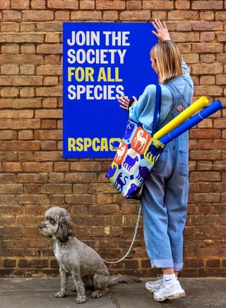 RSPCA new branding poster being put up by woman with dog