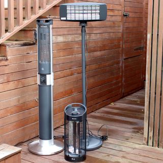 A collection of three patio heaters of different sizes and shapes on wooden decking