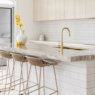 white kitchen with bamboo tiles and gold tap and brass stools