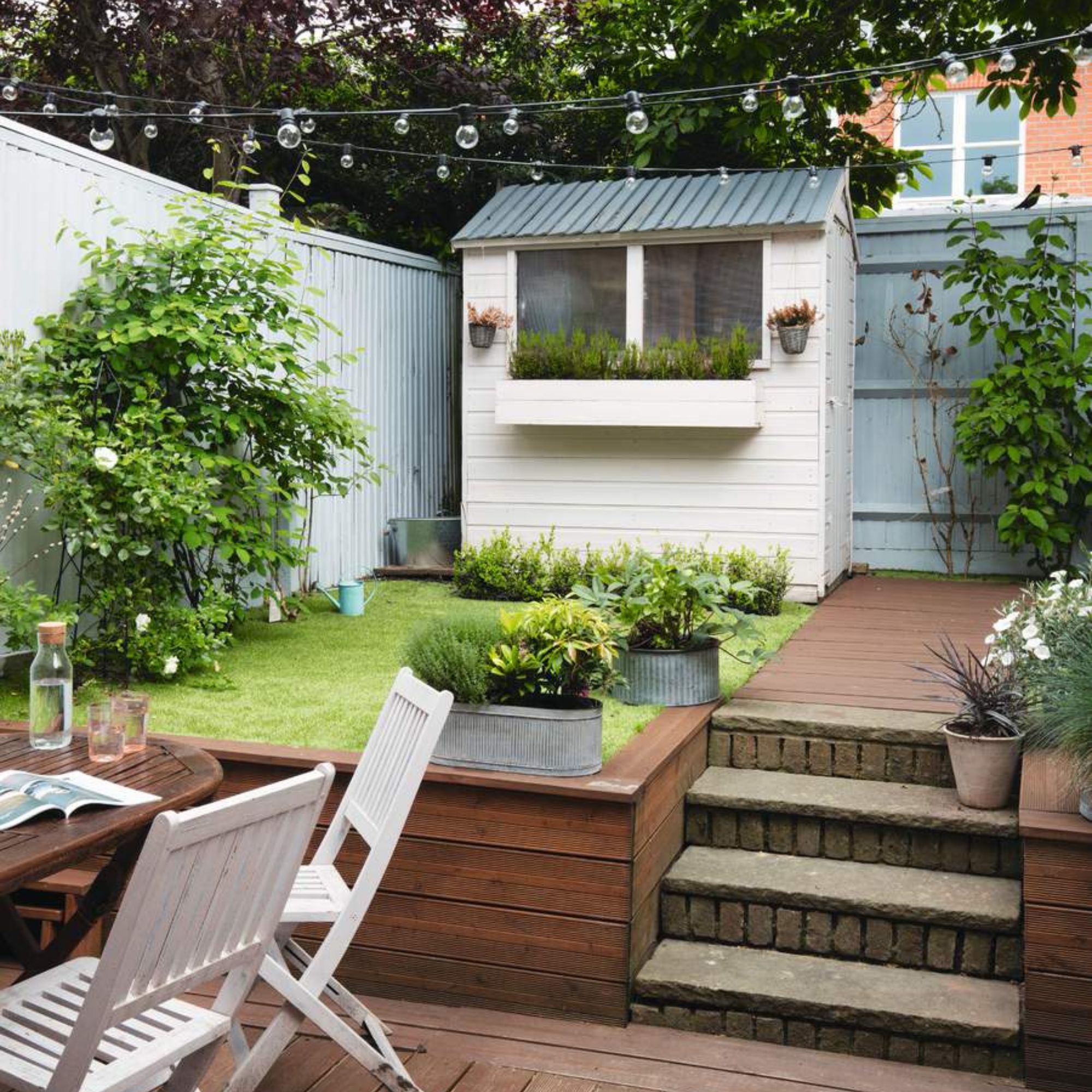 Garden with dining set on the patio, a raised lawn area and a small shed at the back