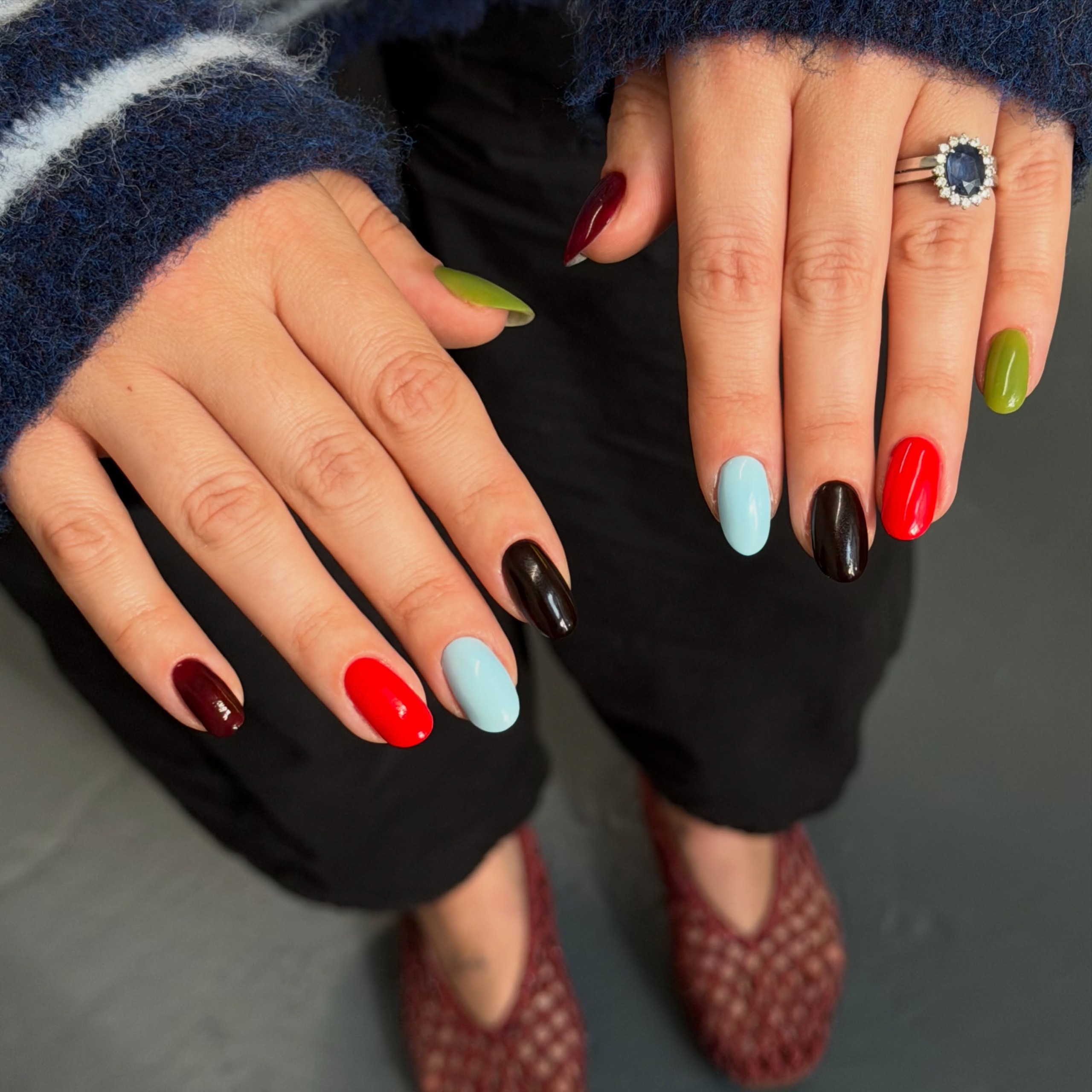 Hands with mismatched red, pale blue, olive and dark-colored nails beside a striped sweater