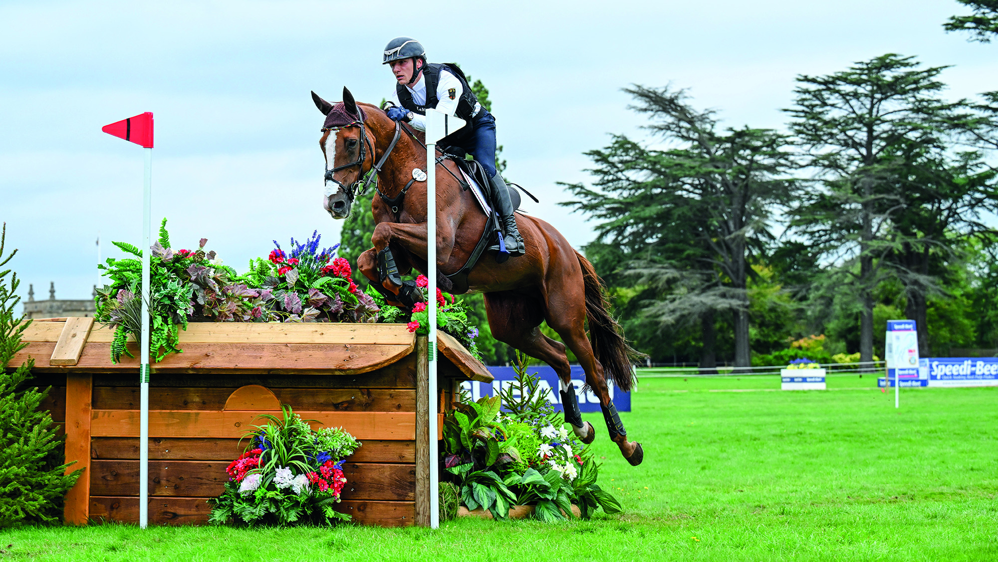 Calvin B&ouml;ckmann, a German rider in black and white colours, rides chestnut horse Phantom Of The Opera over a corner fence on the Blenheim cross-country course at the 2025 European Championships