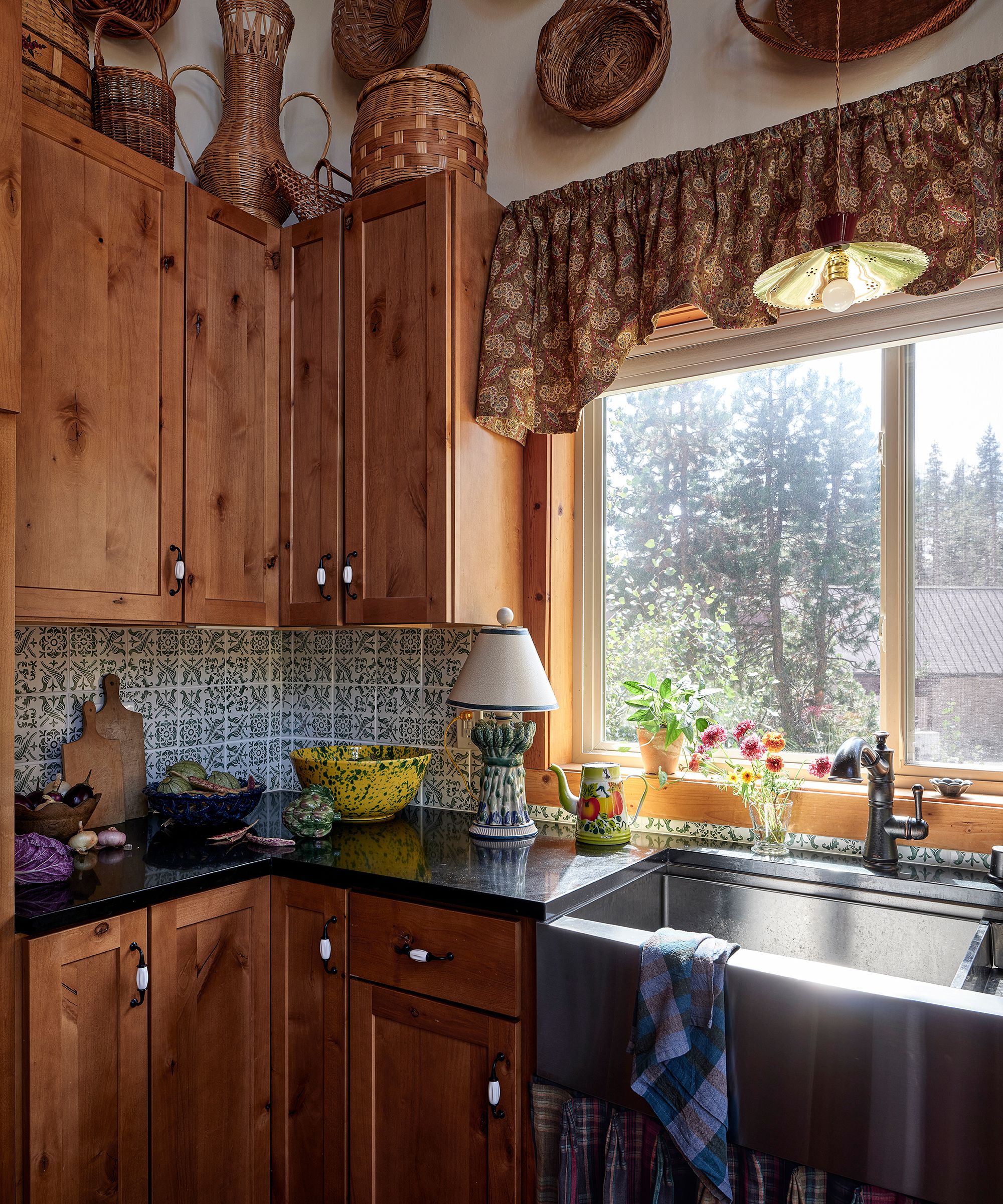 a vintage style wooden kitchen in a ski home with a stainless steel sink, sink skirt and a collection of vintage baskets