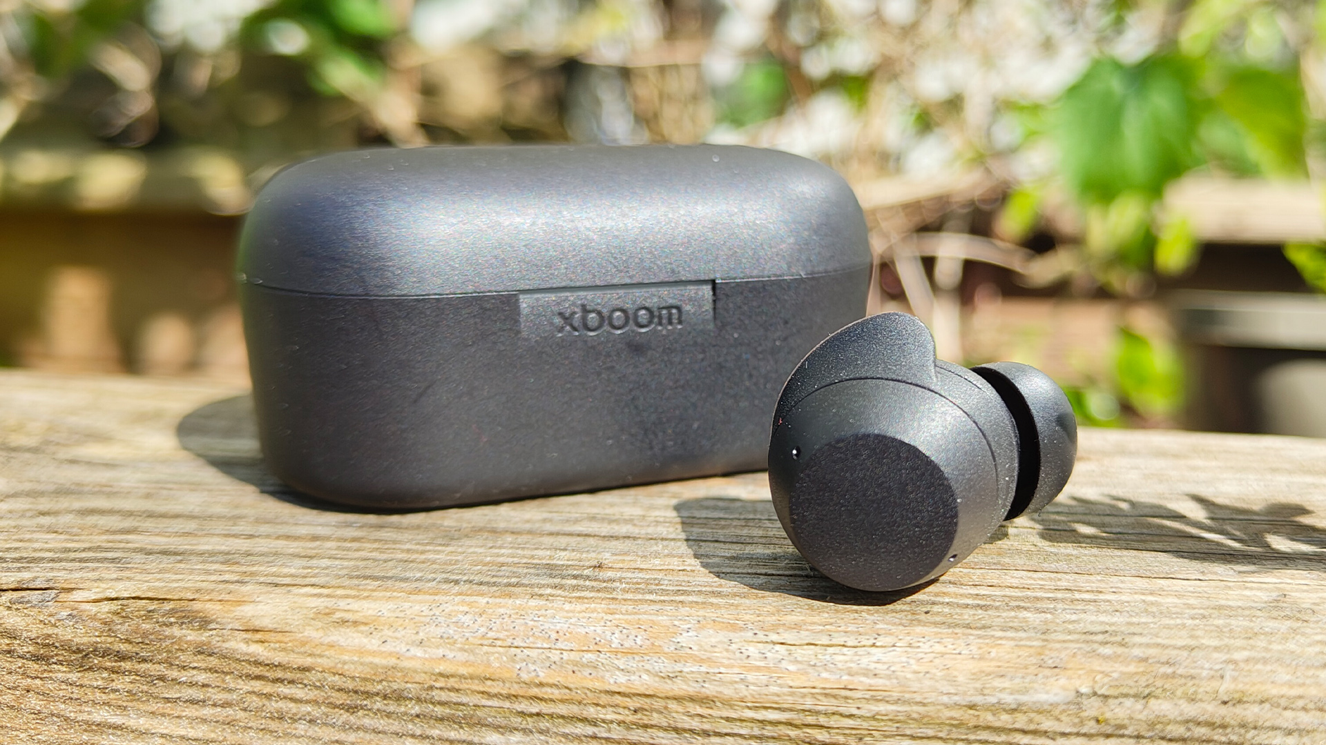 LG Xboom Buds 2025 wireless earbuds one earbud next to charging case on wooden table in sunshine