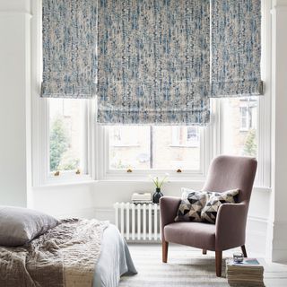 Blue watercolor roman shades over bay window with white painted floor boards and accent armchair