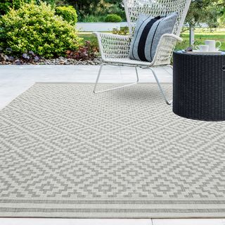 Grey geometric outdoor rug on a white patio in a garden