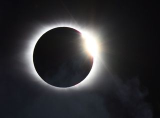 photograph of a solar eclipse where a white outline is visible around a central black circle with a bright light shining from behind the upper right corner.