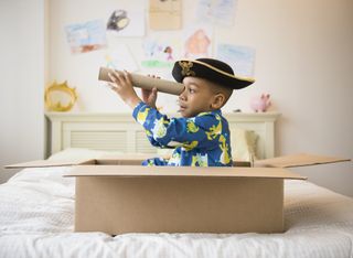 Young boy with a pirate hat and a cardboard telescope playing in a cardboard box