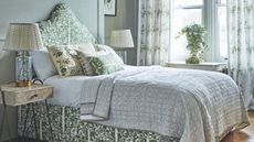 Green patterned bedroom with green patterned bed and cushions and large windows and white patterned curtains