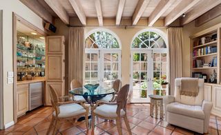 A room with terracotta floor tiles, an armchair, exposed beams and a small round dining table