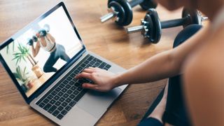 Woman following home weights training video on laptop