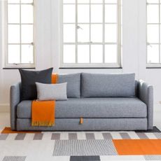 Heal's Oswald sofa bed in grey with an orange throw and grey pillows