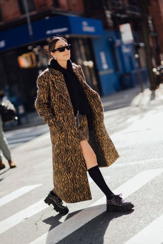 woman wearing animal print coat, skirt, hoodie, sneakers, and high-knee socks