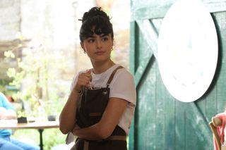 Zoe (Melina Sinadinou) stands in the doorway at Ten Mile Kitchen, absentmindedly poking a pencil down the front of her apron