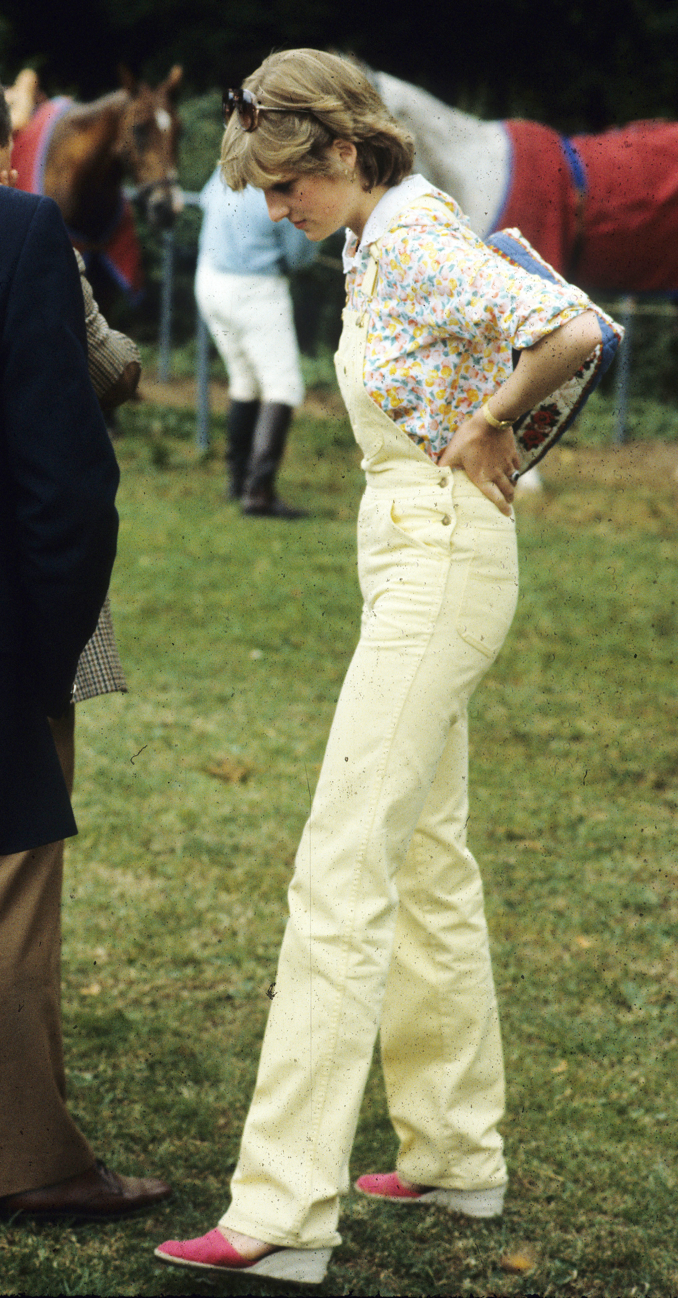 Princess Diana wearing yellow overalls standing in a grass field