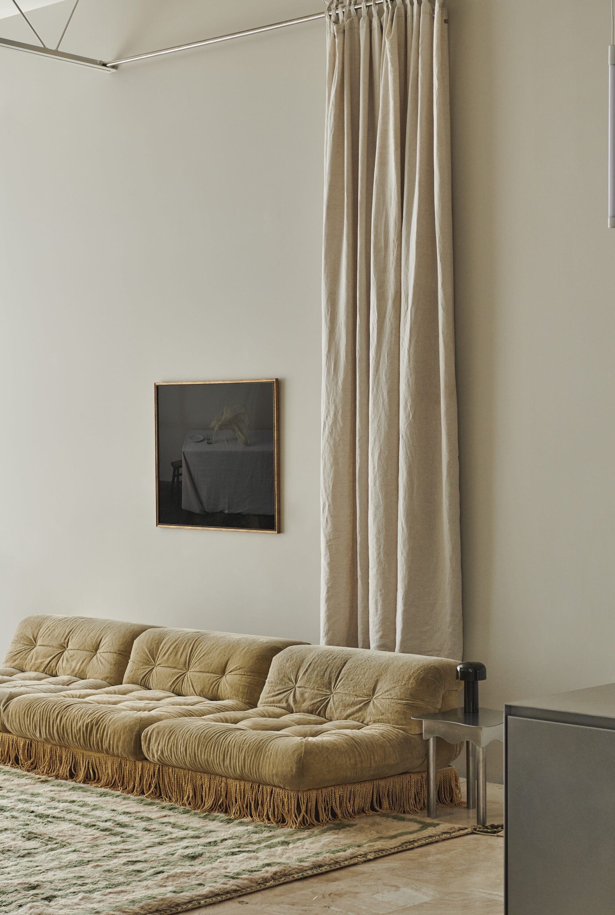 modern living room with artwork on wall, tall curtain, patterned rug and yellow velvet sofa with fringe detail