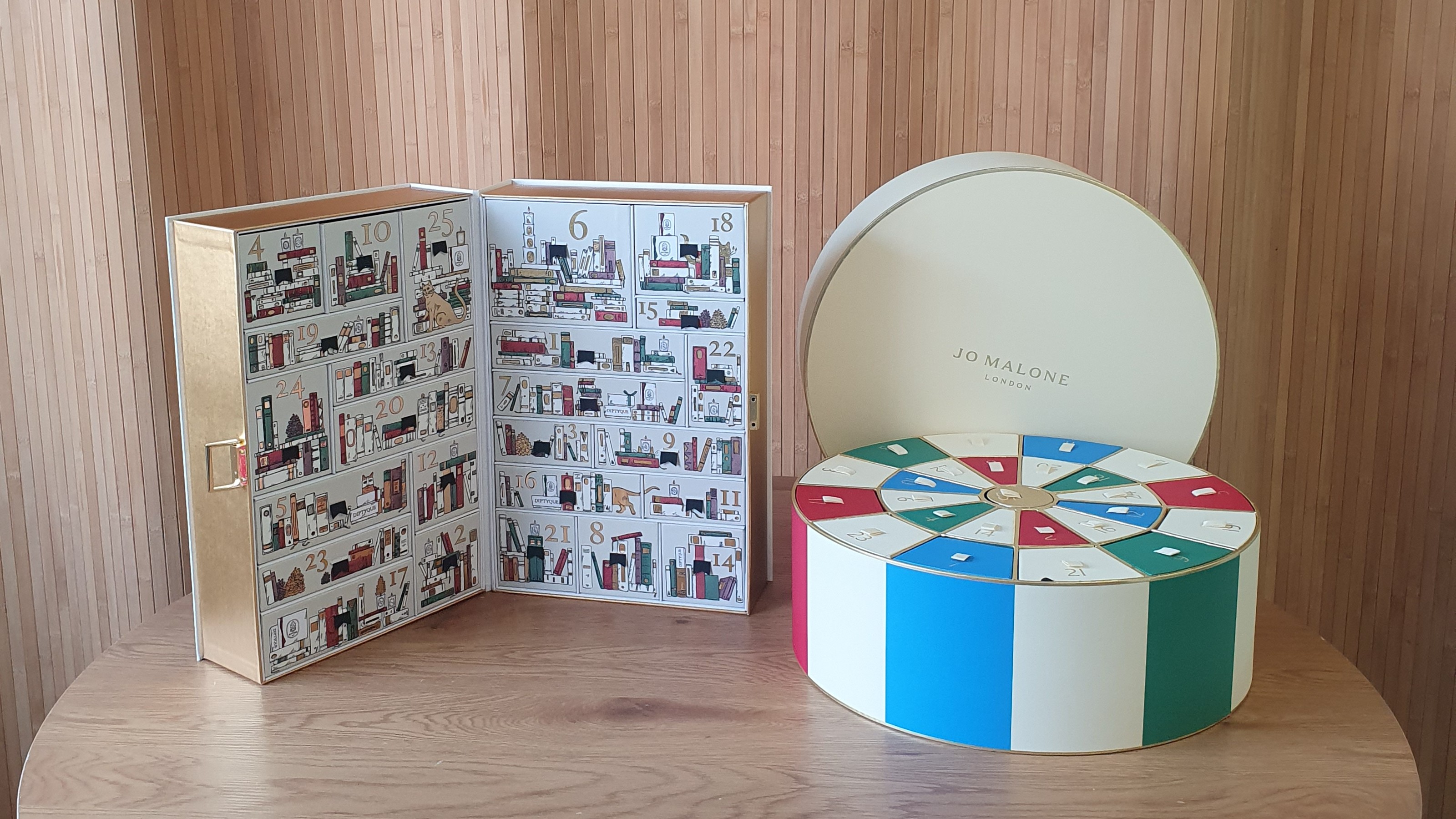 The Diptyque and Jo Malone advent calendars on a wooden table with a panelled backdrop