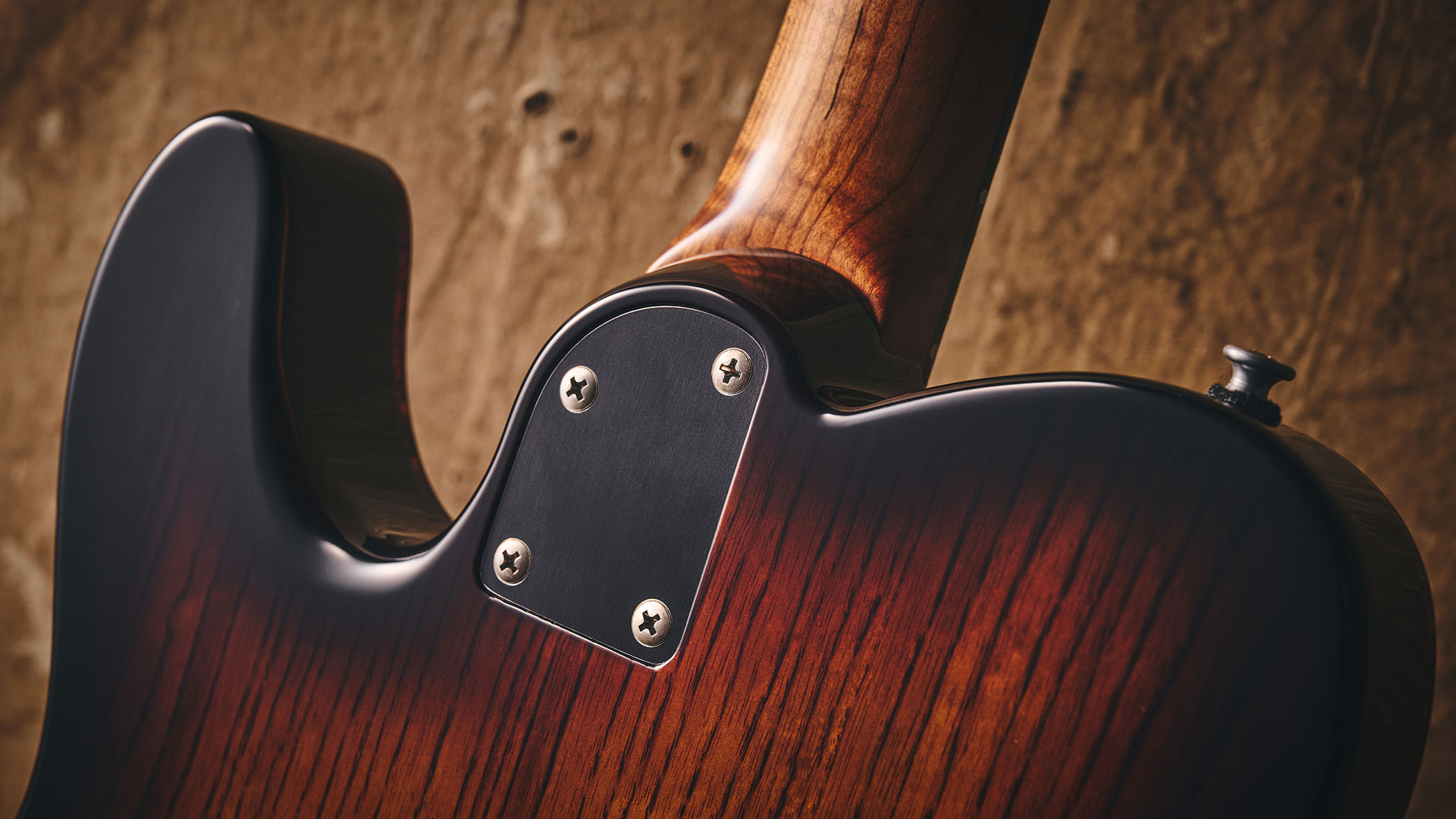 Patrick James Eggle Oz-t Cabronita Thinline; this semi-hollow T-style has a dark sunburst that reveals all the open grain, complementing the tortoiseshell pickguard, and is photographed here against a distressed floor, white and wooden backgrounds.