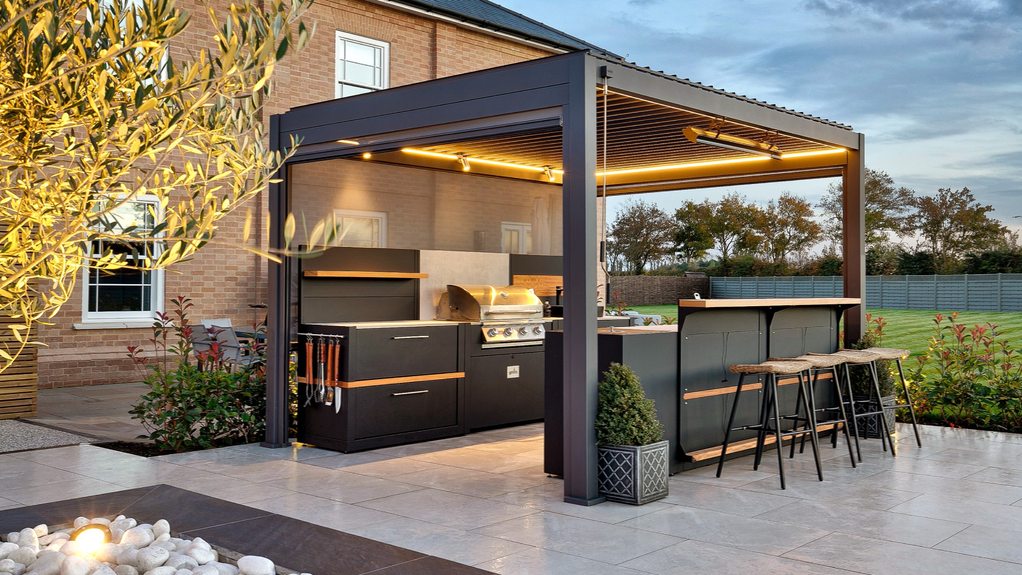 outdoor kitchen and BBQ area under dark grey aluminium framed pergola with louvered roof