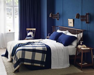 A bedroom with navy blue wall, brown wooden bed and white and navy bed linen