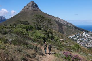 Prince William walking in front of a towering seaside mountain with a woman