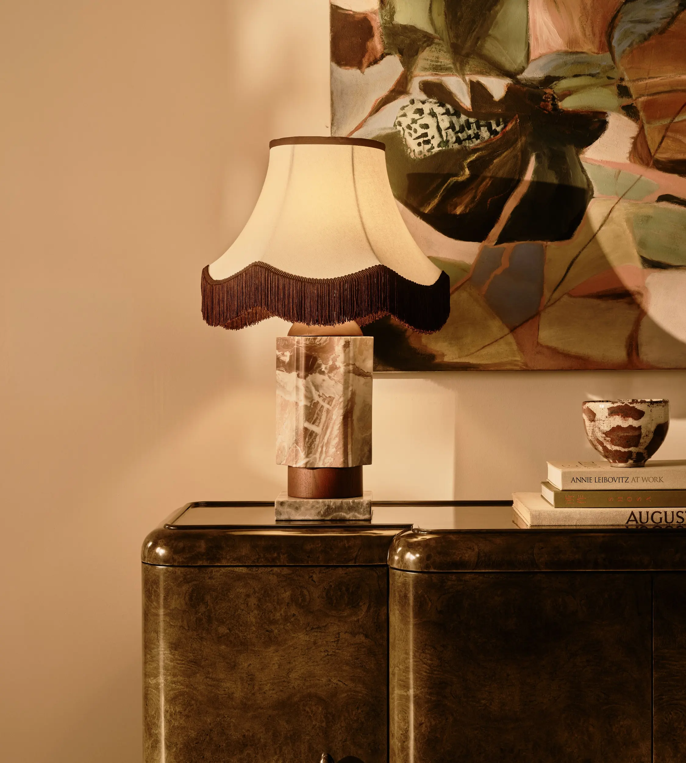 soho home table lamp with tassels on a burl console next to a pile of books in front of a large colorful artwork on the wall