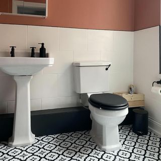 bathroom showing toilet with black lid and sink against white wall tiles and orange wall