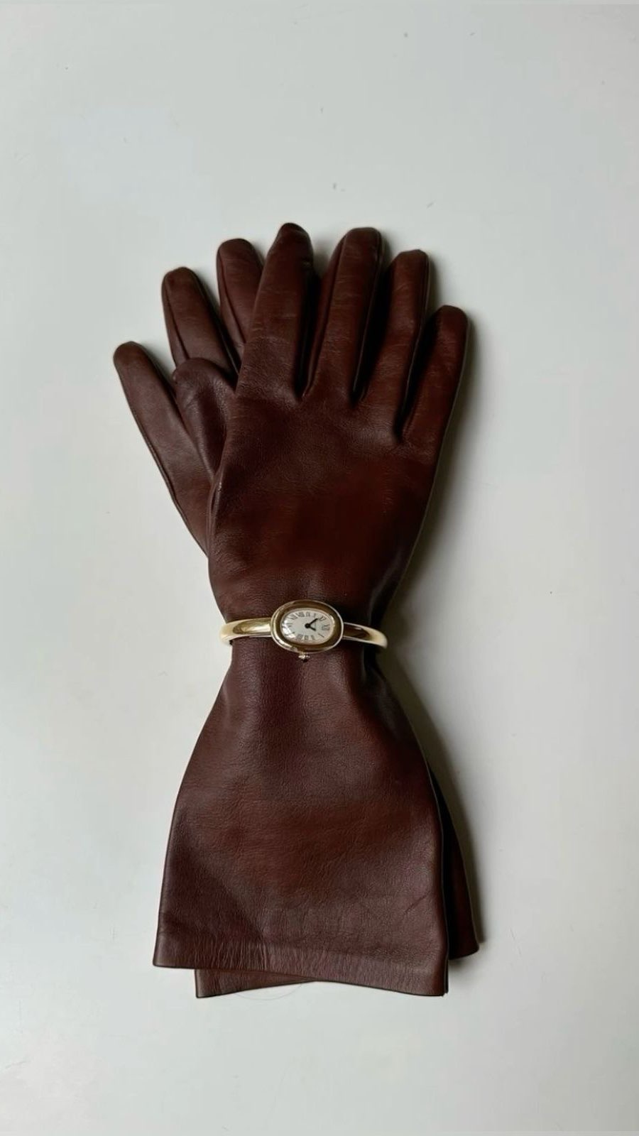 An image of a pair of burgundy leather gloves held together by the Cartier Baignoire watch.