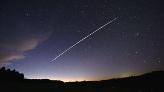 A long-exposure image showing a trail of a group of SpaceX's Starlink satellites passing over the landscape