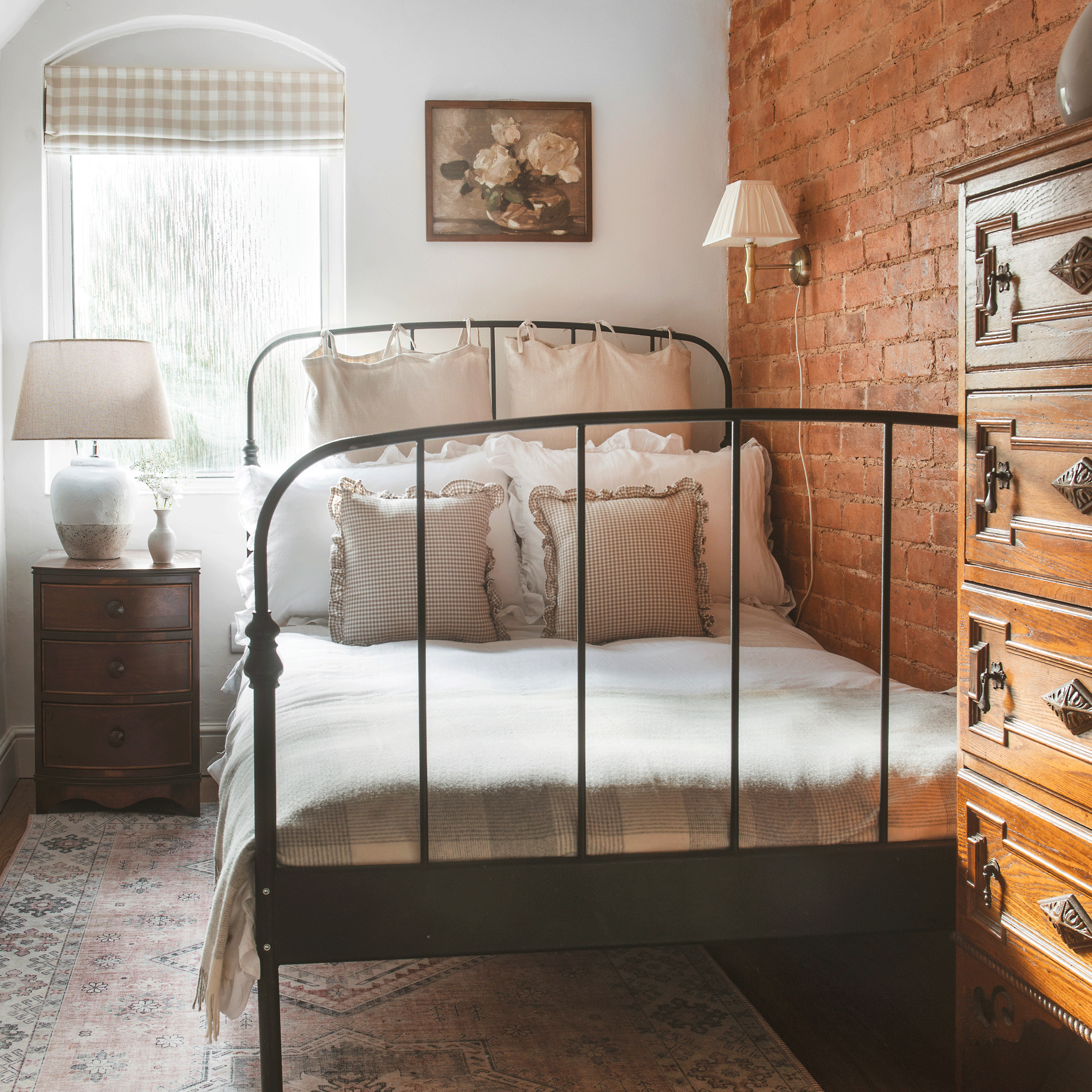a bedroom with a wrought iron bedframe and frill-edged cushions and an exposed brick wall