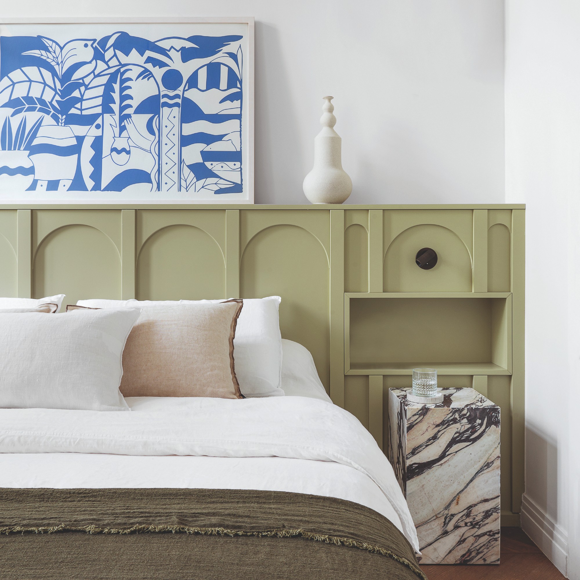 A bedroom with a half-height green wall panelling, white-painted walls and a blue artwork