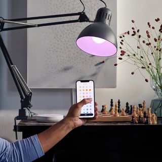 IKEA DIRIGERA smart home hub on a desk with a lamp, with someone operating it from their phone