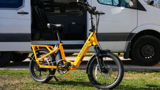 Velotric Fold 1 Plus ebike outdoors in front of white van on grass