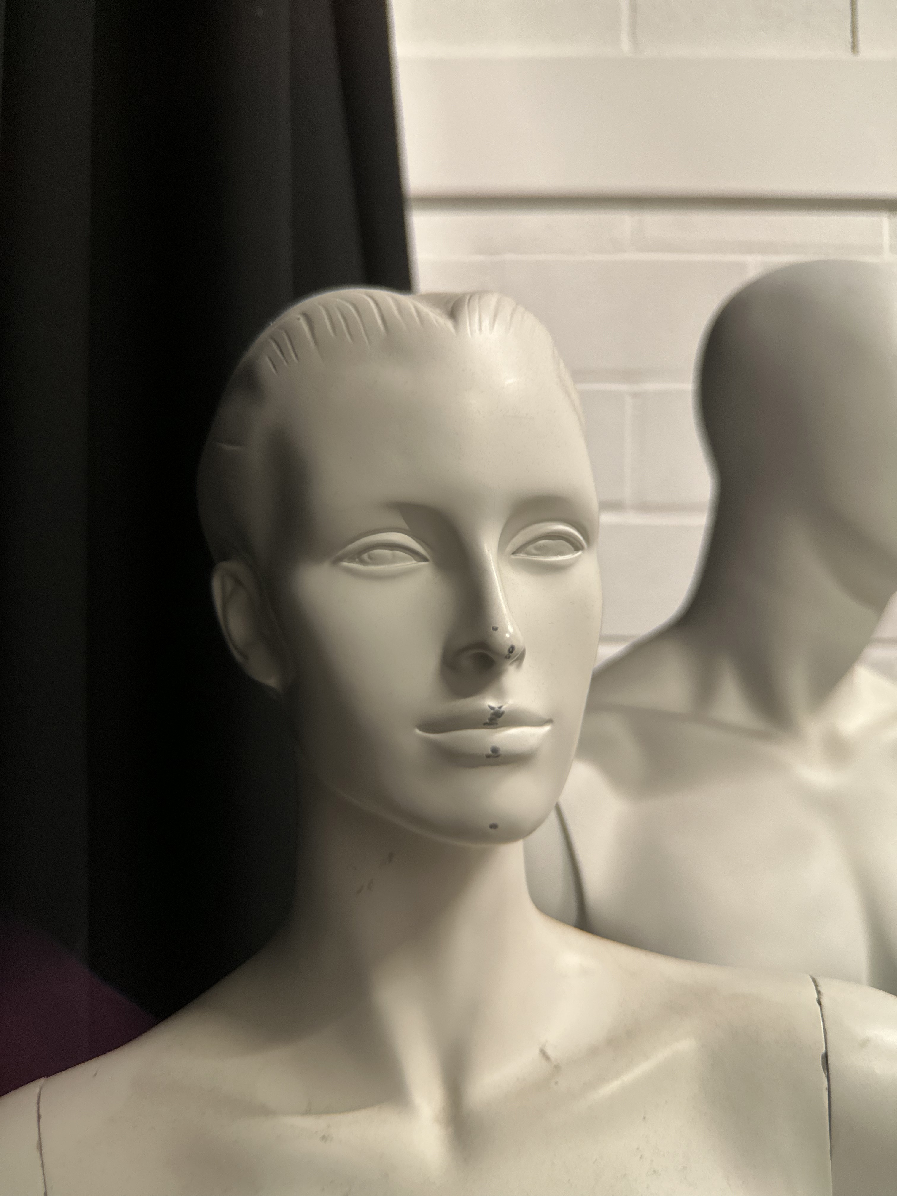 A photo of a white mannequin with a black curtain and white wall in the background.